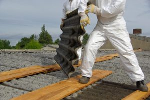 Trained asbestos removal contractors in protective suits carefully removing corrugated asbestos sheets from a roof in Crawley.
