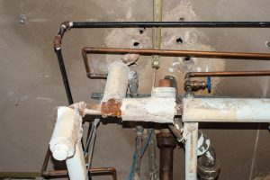Old heating system pipes with damaged insulation that may contain asbestos in an ageing building.